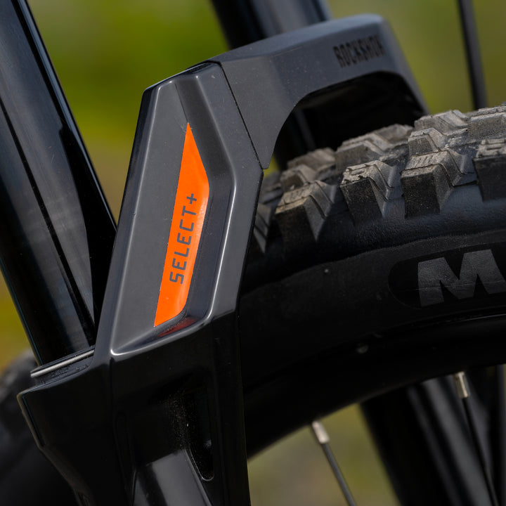 Close-up of a black RockShox ZEB Select+ bicycle fork with an orange accent panel labeled &