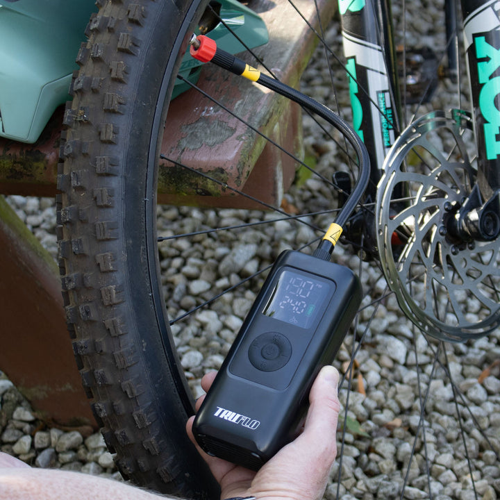 Person using a Truflo digital pump on a mountain bike tyres outdoors.
