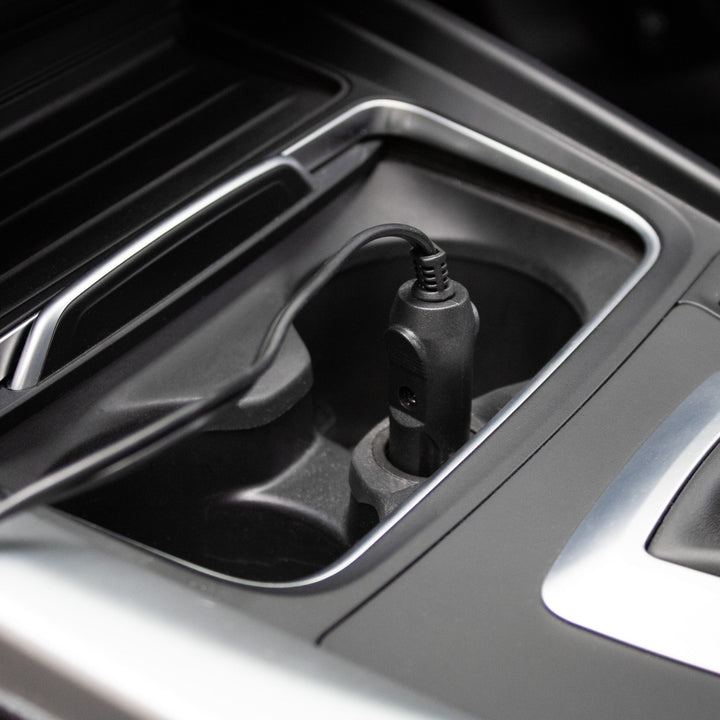 Car charging port with a cable plugged in on a car dashboard.
